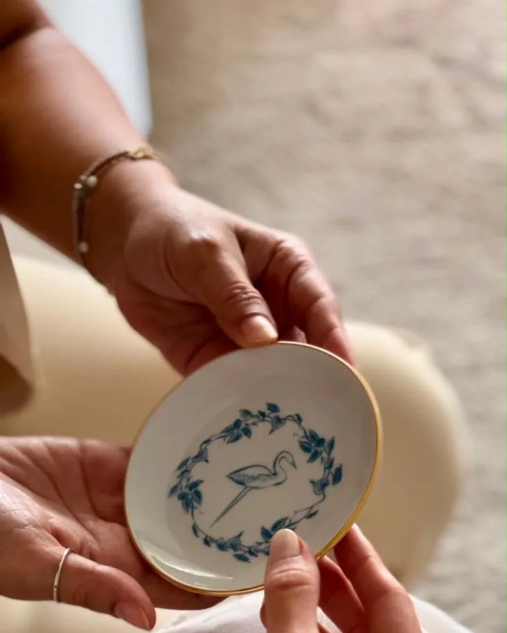 Mãos segurando um descanso de joias de porcelana com coroa de ramos e beija-flor em azul