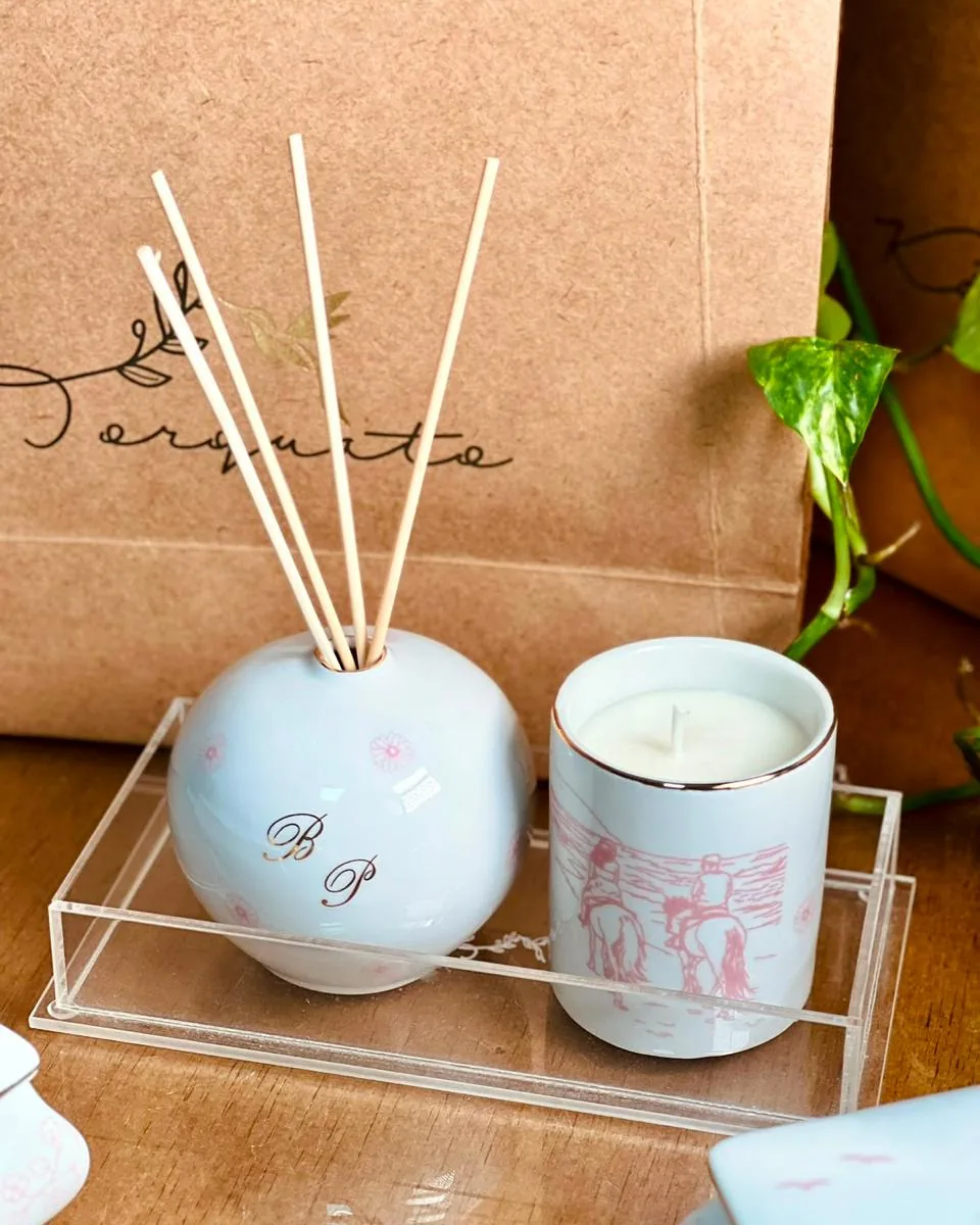 Kit home com difusor e vela em porcelana com toile rosa sobre bandeja de acrílico, sacola kraft ao fundo