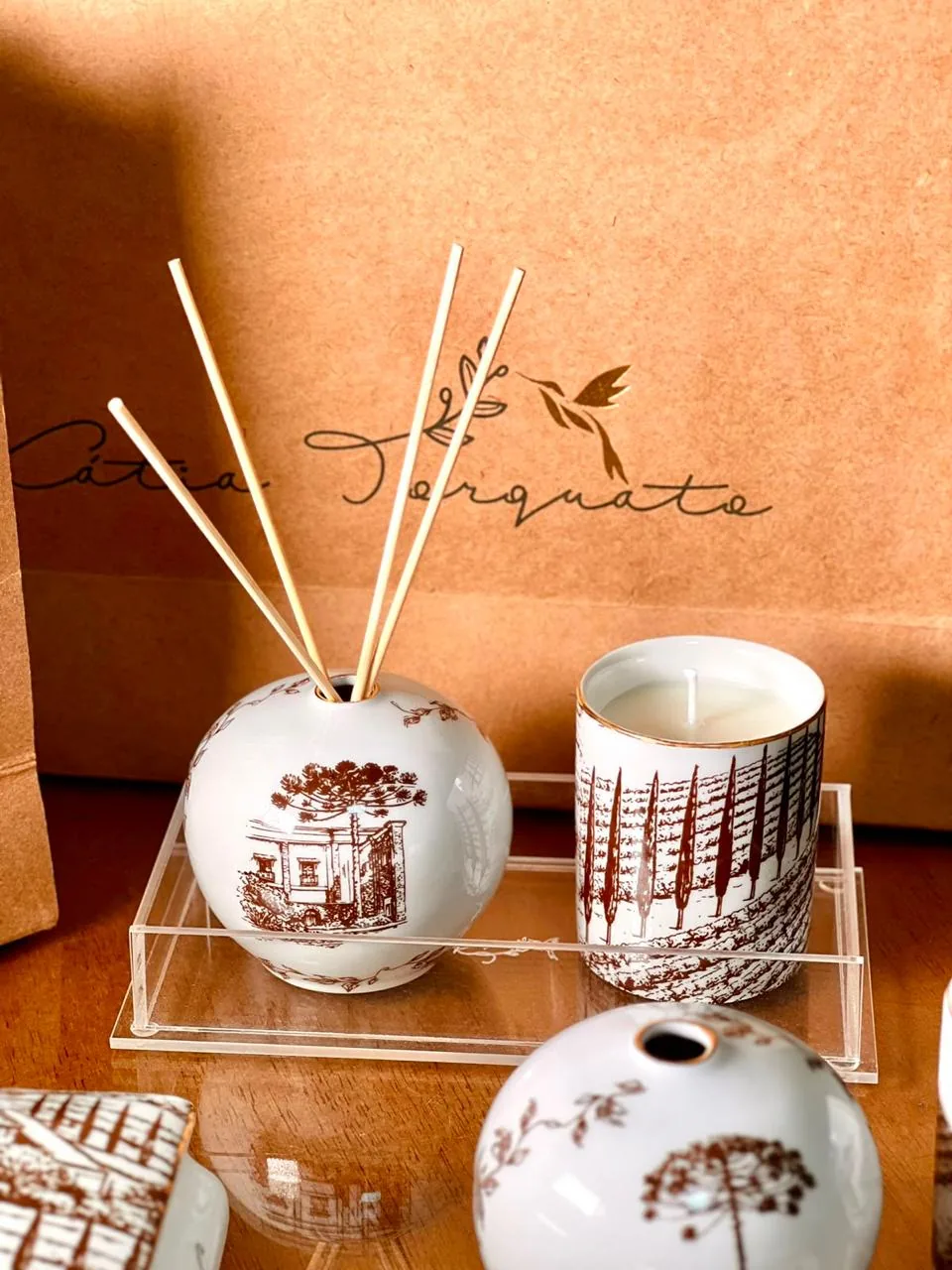 Difusor com paisagem e vela com casario em sépia, sacola kraft com a logo do ateliê